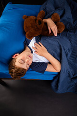 Young boy sleeping near the edge of his bed while holding his teddy bear