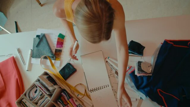 Top down view on messy table of creative professional, fashion designer make sketches and drawings of new model in notebook. Small business owner, slow fashion and recycling