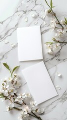 a mockup featuring two blank white invitation cards placed side by side on a light marble surface, with white flowers, captured from a top view, generous space for text or design elements.