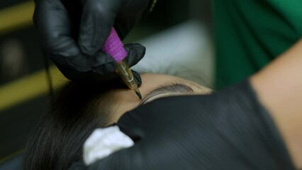 Close up microblading eyebrow tattoo. Beautician in gloves makes permanent makeup correction of the shape of the eyebrows to a young women. Eyebrow tattoo in a beauty salon.