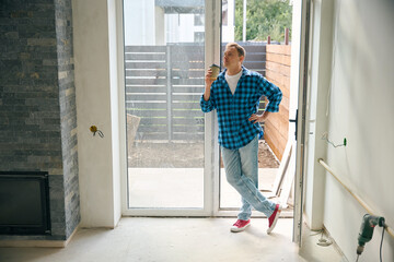 Fototapeta premium Man standing near door and drinking coffee from paper glass