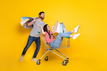 Full length photo of couple wear t-shirt hold shoppings bags girl sit in cart look at sale empty...