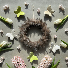 A feather wreath with spring flowers, overhead view on grey stone background. White tulips, pink...
