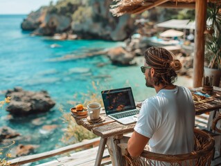 Man engrossed in remote work on laptop at a wooden desk, overlooking a scenic rocky ocean landscape