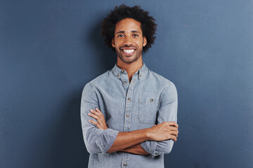 Portrait, smile and black man with arms crossed, fashion and afro on a blue studio background....