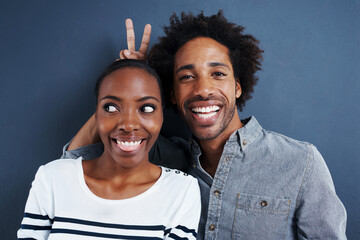 Happy, portrait and black couple with peace and love on studio background together with happiness. Crazy, face and sign for bunny ears in silly profile picture of people with casual fashion or style