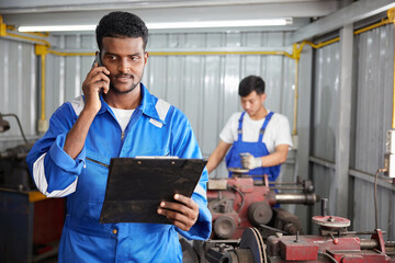 worker or technician talking on smartphone with customer and holding a clipboard in the factory