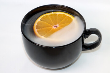 hot tea with oranges from which it is smoking in a black mug on a white background