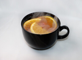 hot tea with oranges from which it is smoking in a black mug on a white background