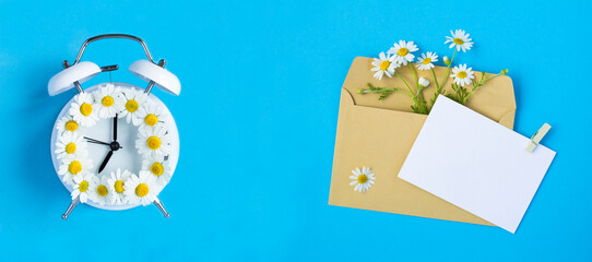 White alarm clock with chamomile and empty white paper for text on the blue background. Copy space....