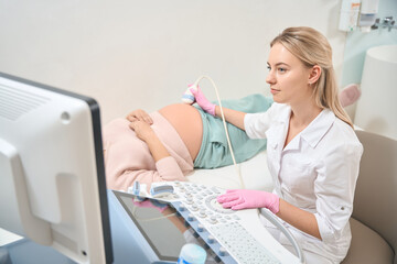 Young qualified sonographer making ultrasound to pregnant woman