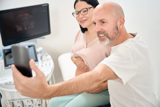 Spouses making selfie on background of ultrasound image of baby