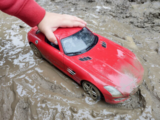 A child plays with a red toy car in the mud