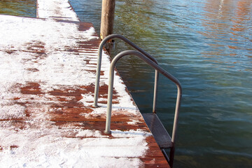 Small wooden pier in the snow with stairs to Lake Traunsee in Austria.