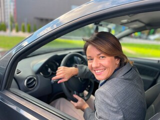 Close up shot of joyful beautiful business lady sitting in own auto and smiling at camera. Positive happy Caucasian woman driving a car in good mood. Business woman concept