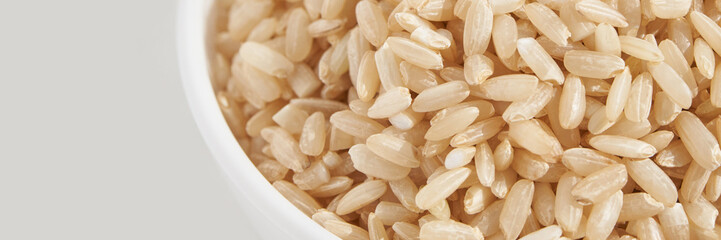 A bowl of uncooked brown rice, isolated against a white background. Healthy, savory dish includes whole grains like jasmine and basmati, showcasing a dieting Asian cuisine. Horizontal banner