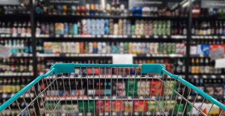 Green shopping cart with blurred image of alcohol store in background. (Selective focused at...