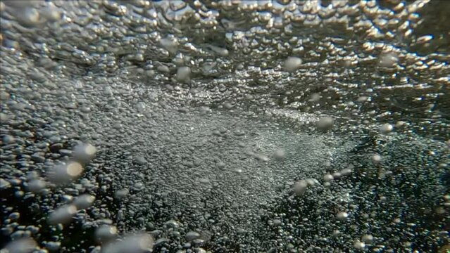Camera slowly descends to subsurface in fast current of fresh water mixed with air bubbles flowing into sea, Split level underwater shot, Slow motion, Mouth of mountain river flows into sea