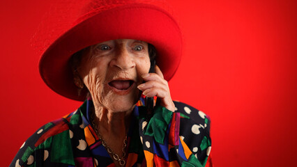 Funny closeup view of toothless old elderly woman wearing red hat isolated on red background...