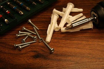 Tools and fasteners on a wooden surface. Dowels, screws, screwdriver, bit set. 