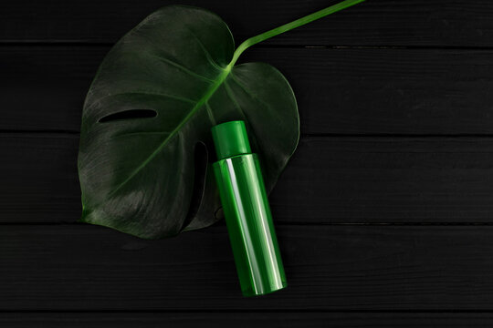 Зелена пластикова бутилка з косметикою без написів та етикеток на темному деревяному столі з листком пальми
