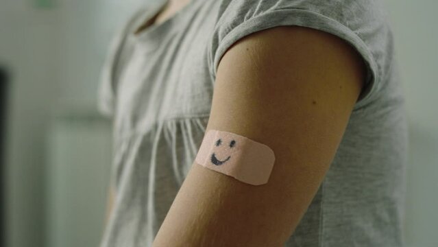 Close up of a doctor's hand putting plaster on a little girl's arm.
the patch has the design of a smiley face.
Prevention, medicine and vaccines concept.