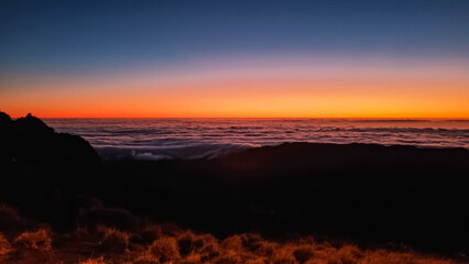 Panoramic view of sunrise seen from top Pico do Areeiro, Madeira island, Portugal, Europe. First sunlight touching surface of illuminated clouds covering the Atlantic Ocean. Dramatic red orange sky