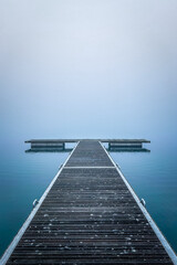 Pier on the water of a lake invaded by a thick fog, blue predominance, blue water 