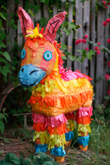 cute colored pinata donkey in the garden against the background of a fence and flowers Cinco De Mayo holiday tradition to Mexico