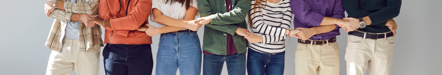 Cropped photo of young people friends students or company employees men and women wearing casual clothes holding hands standing together in a row on a gray wall background. Banner. - Powered by Adobe