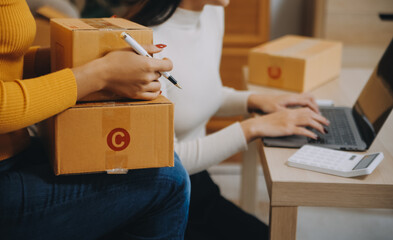 Asian SME business women use laptop computer checking customer order online shipping boxes at home....