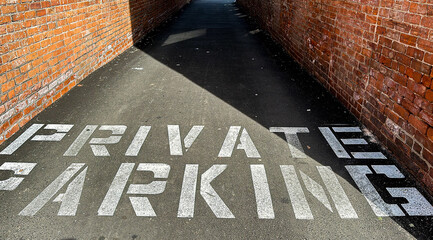 Private parking text painted on asphalt walkway between brick walls with available copy space - obrazy, fototapety, plakaty