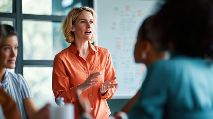 Female professionals are engaged in a discussion, with one of them gesturing expressively, likely explaining or presenting a concept with a whiteboard full of graphs and data in the background.