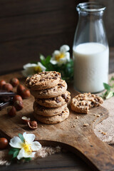 Chocolate chip cookies with nuts, bottle of milk and white flowers on wooden background. Side view. Still life concept
