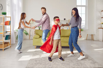 Full length photo of a happy family having fun with children in the living room at home. Child boy in superhero costume dancing with hir mother indoors. Family time and leisure concept.