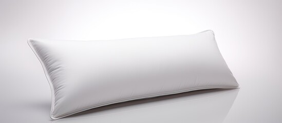 A white rectangular pillow is placed on a white paper surface, creating a monochrome composition. The sleek design resembles a fashion accessory