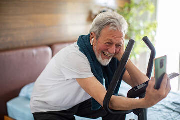 Senior man using smartphone on fitness bike at home