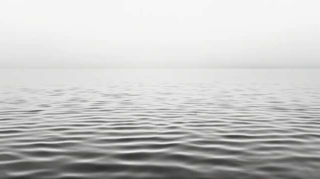  a black and white photo of a large body of water with ripples on the water and a foggy sky in the background.