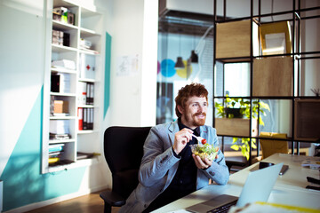 Young businessman eating a salad in the modern office