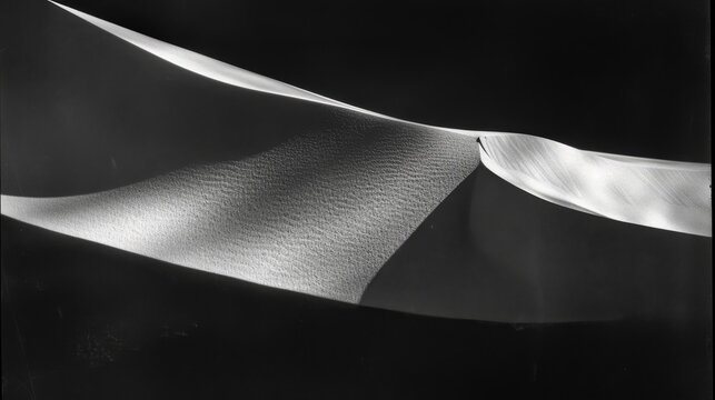  a black and white photo of a sand dune with a long white ribbon hanging from the top of the dune.