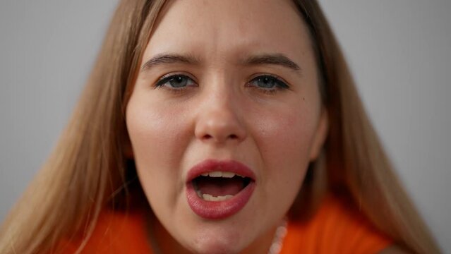 Portrait of young stressed shouting girl. Isolated excited young woman in orange t-shirt screaming raising hands opening mouth closing eyes in studio indoors. Joy, surprise, amazement, panic concept.
