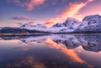 Beautiful snowy mountains and colorful sky with clouds at sunset in winter in Lofoten islands, Norway. Landscape with rocks in snow, sea coast, reflection in water at dusk, purple sky with pink clouds - 758232434