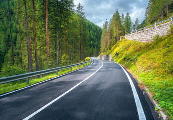 Road in green forest at sunset in summer. Dolomites, Italy. Beautiful mountain roadway, tress, grass, high rocks, blue sky with clouds. Landscape with empty highway through the woods in spring. Travel - 758232669