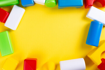 Children's plastic colored blocks, construction set, on yellow background, copy space. Educational baby toy.