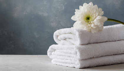 Stack of clean fluffy white towels folded on table. Fresh smelling flower.