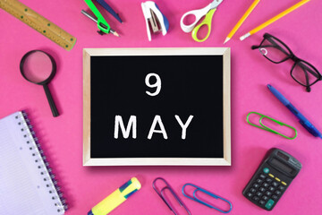 May 9 written in chalk on black board. Calendar date 9th of May on chalkboard on pink blurred...