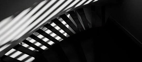 A monochrome photograph of a staircase with shadows creating a fascinating pattern on the wall. The metal railing stands out against the darkness, emphasizing the contrast of tints and shades