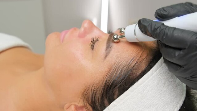 Close-up portrait of a beautiful woman with closed eyes and apparatus for skin rejuvenation. Beauty salon procedures. RF lifting. Microcurrents.