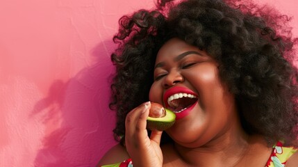 Laughing woman with an avocado half near her mouth on a pink background. Happiness and healthy...