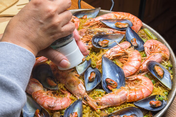 Close-up of a hand seasoning traditional seafood paella with rich colors, typical Spanish cuisine, Majorca, Balearic Islands, Spain